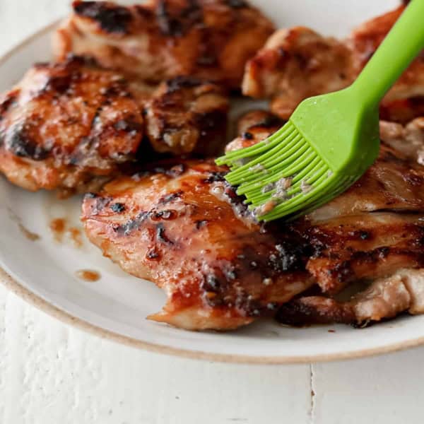 cooked chicken thighs being topped with a garlicky soy sauce