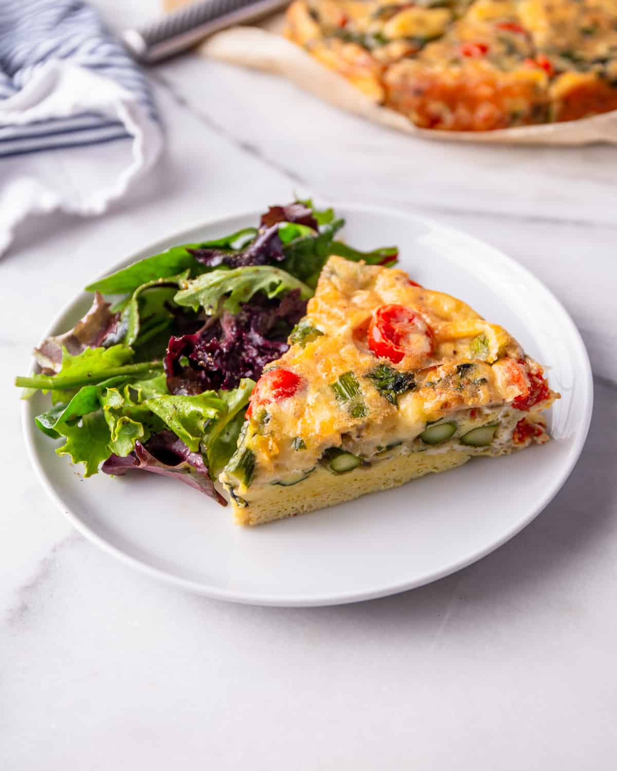 a slice of frittata on a white plate with a green salad