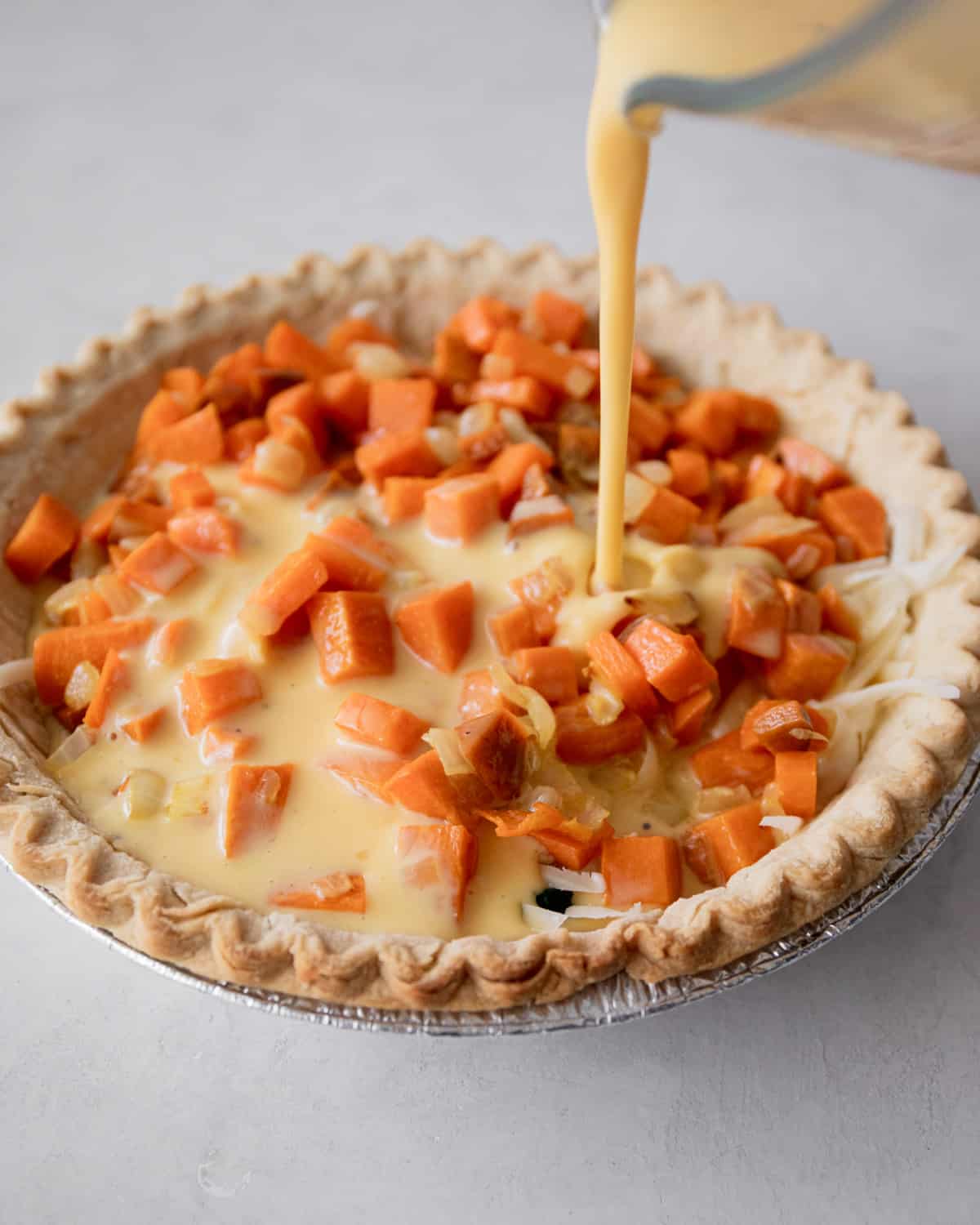 adding egg mixture to vegetables in a pie crust