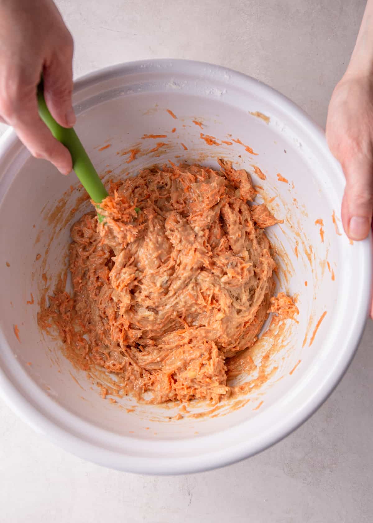 stirring carrot cake muffin mixture in a white mixing bowl