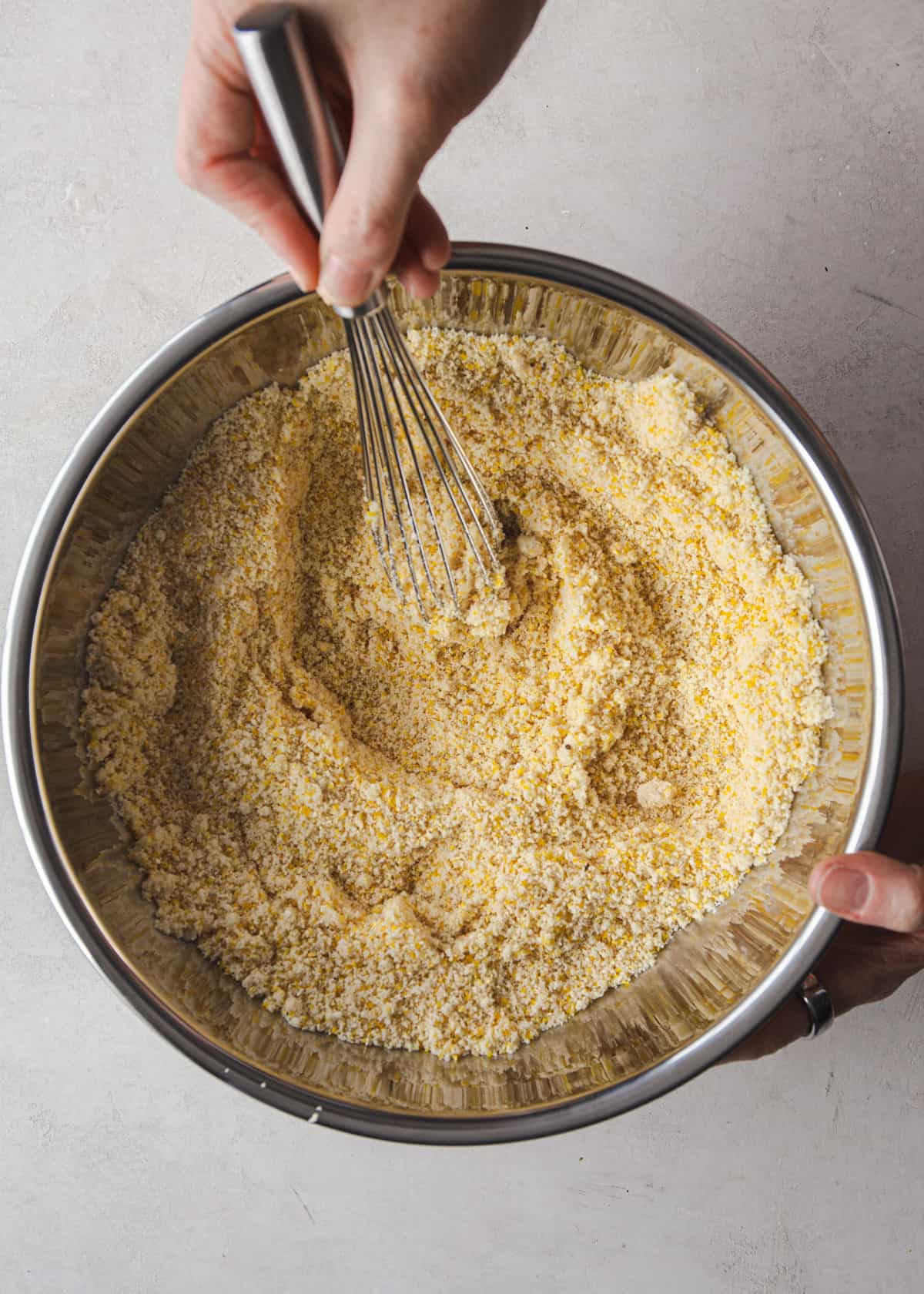 stirring polenta mixture in a silver mixing bowl