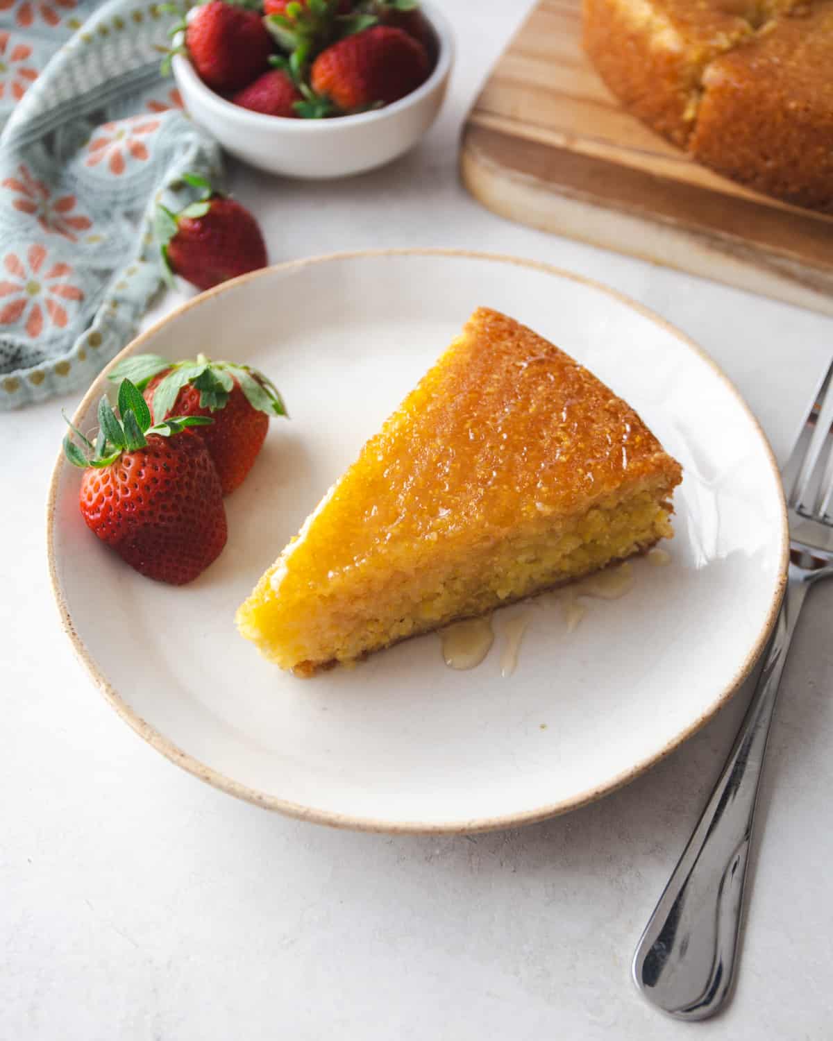 a slice of polenta cake on a white plate with strawberries