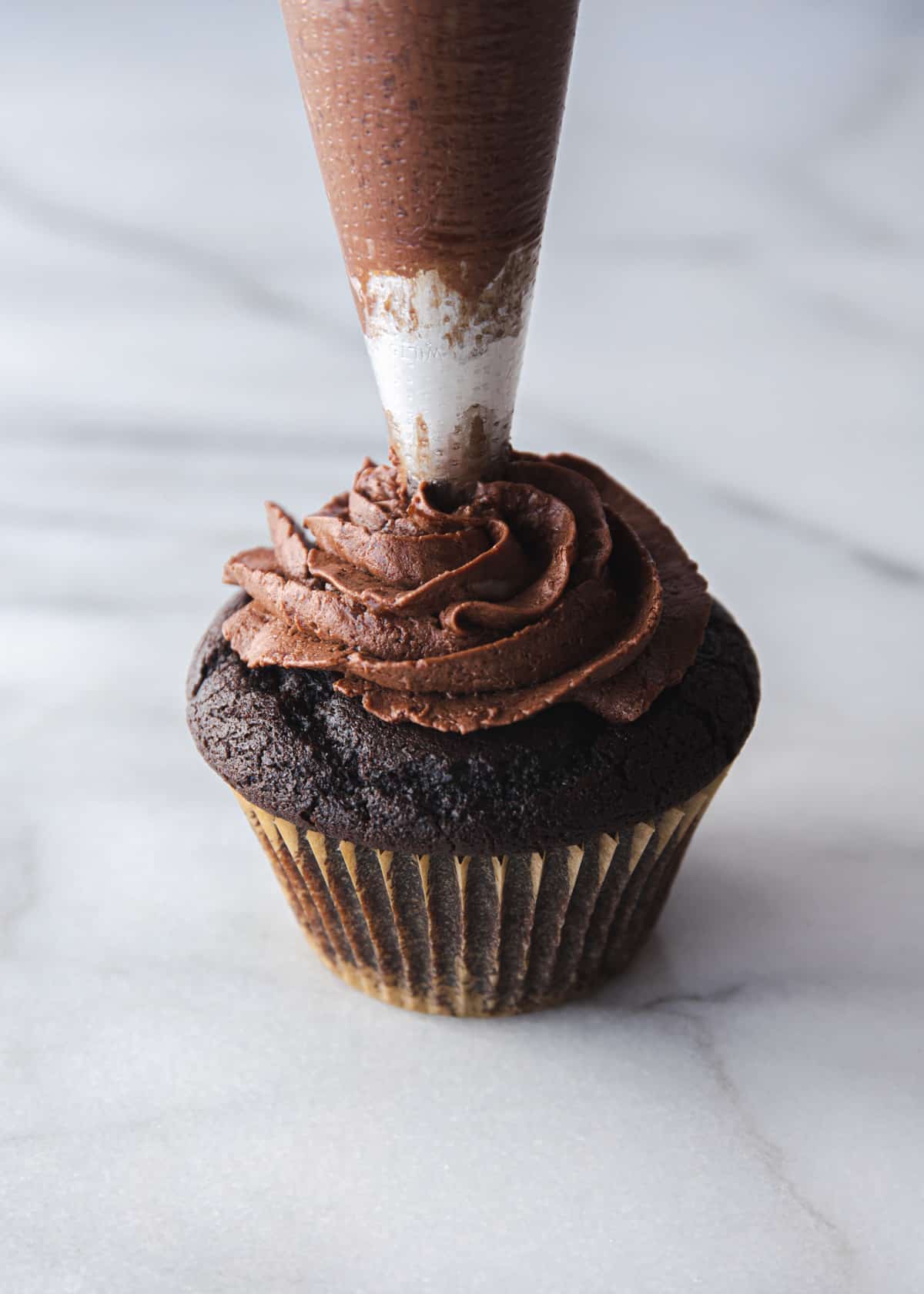 piping frosting on a chocolate cupcake