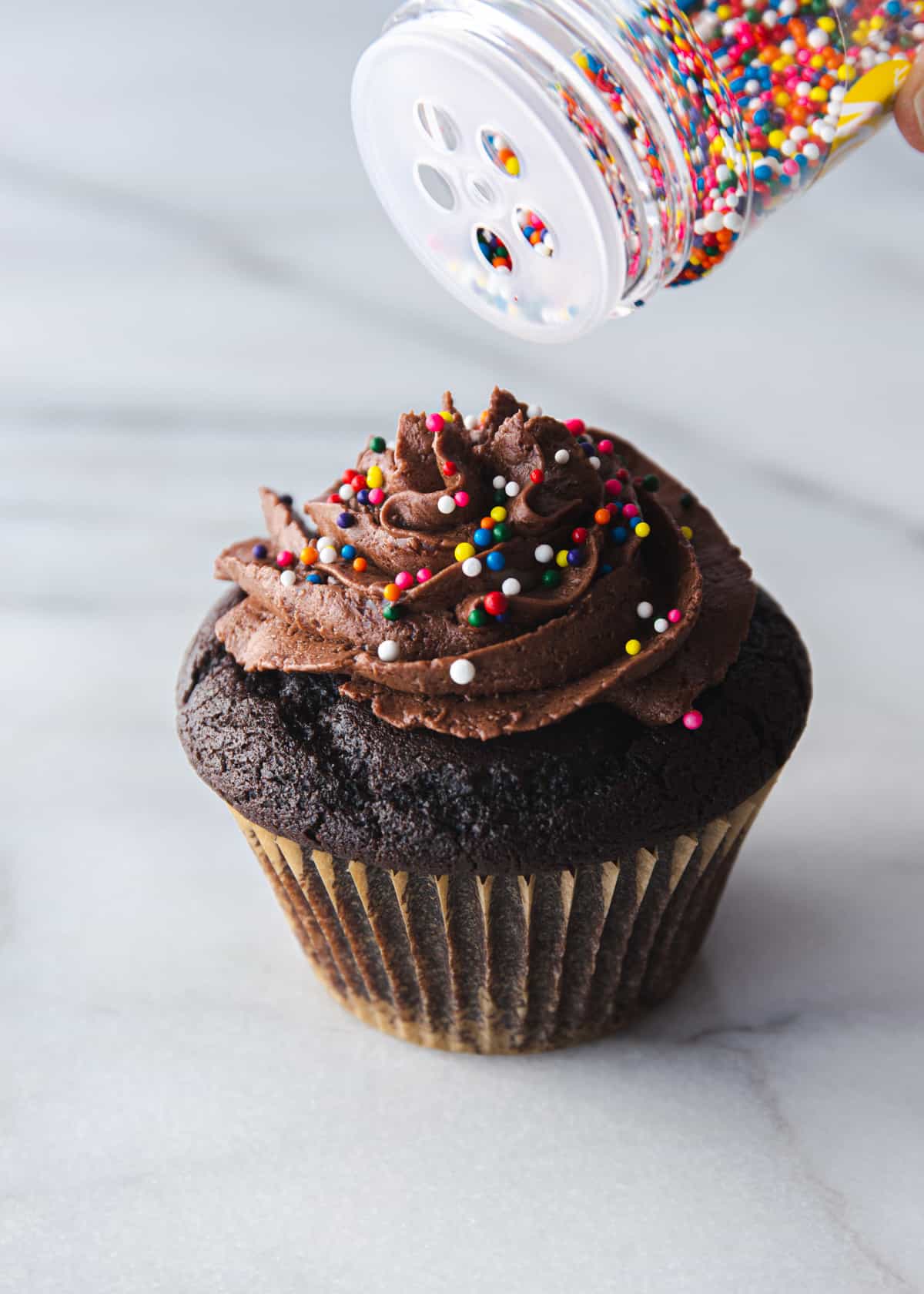 adding sprinkles to the top of a cupcake