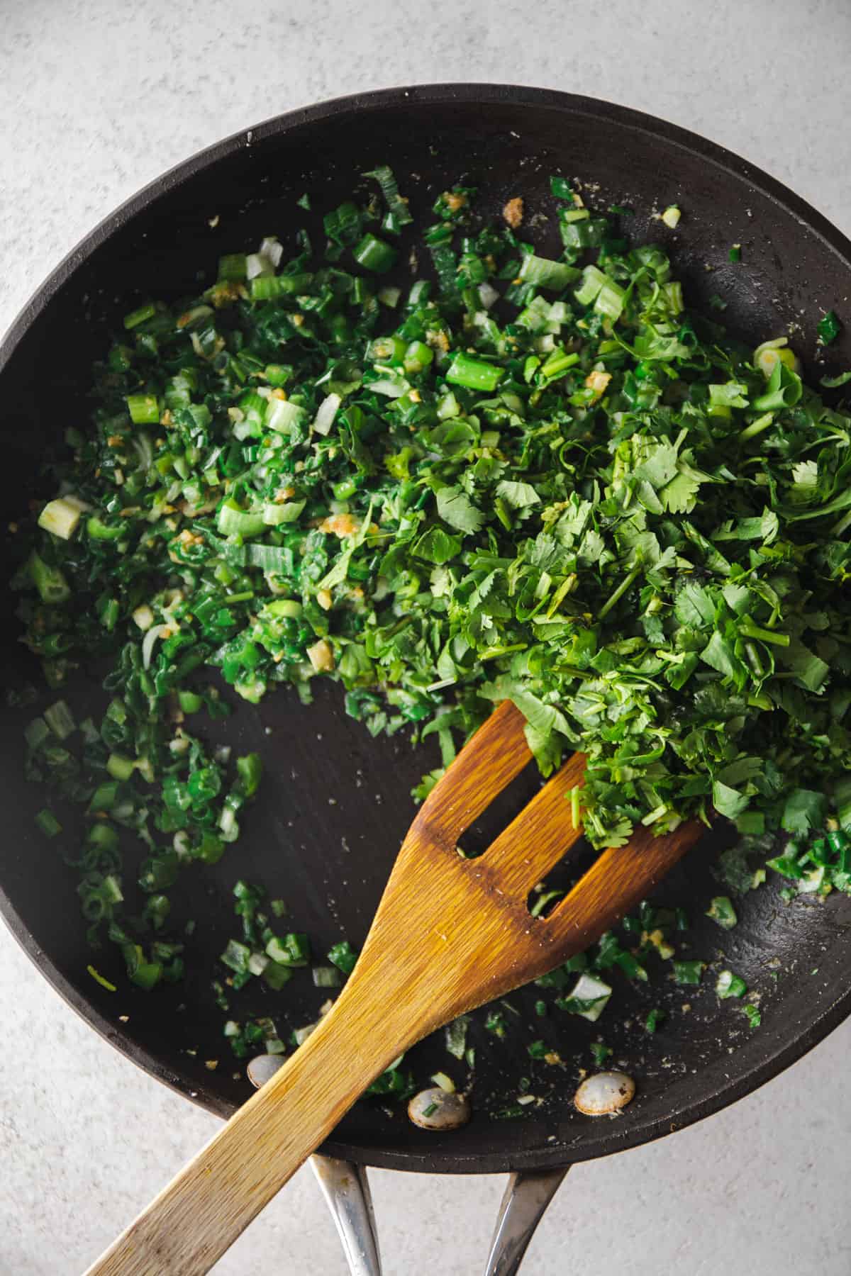 overhead image of stirring scallions in a skillet with a wooden spoon