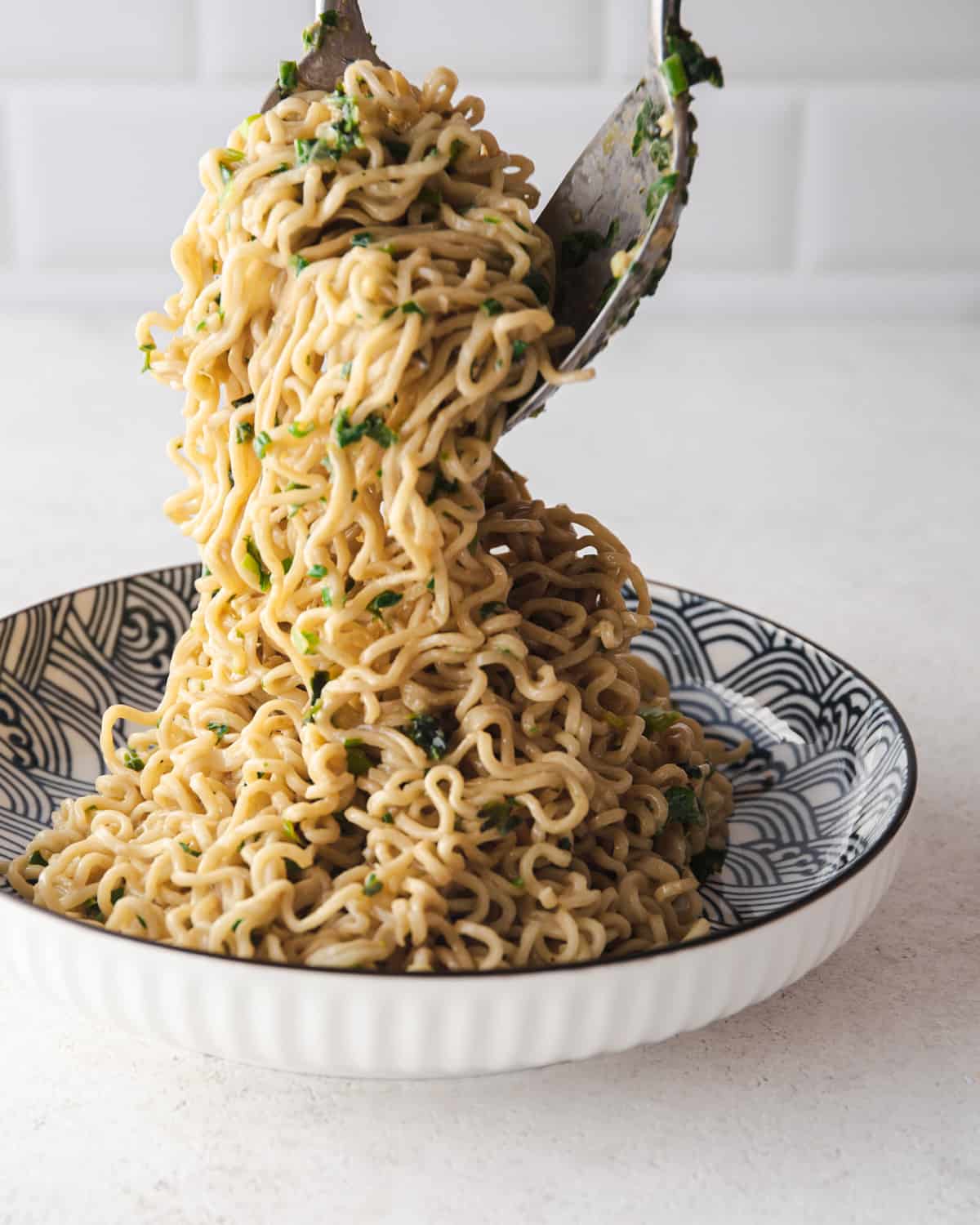 spooning miso scallion noodles out of a blue and white bowl
