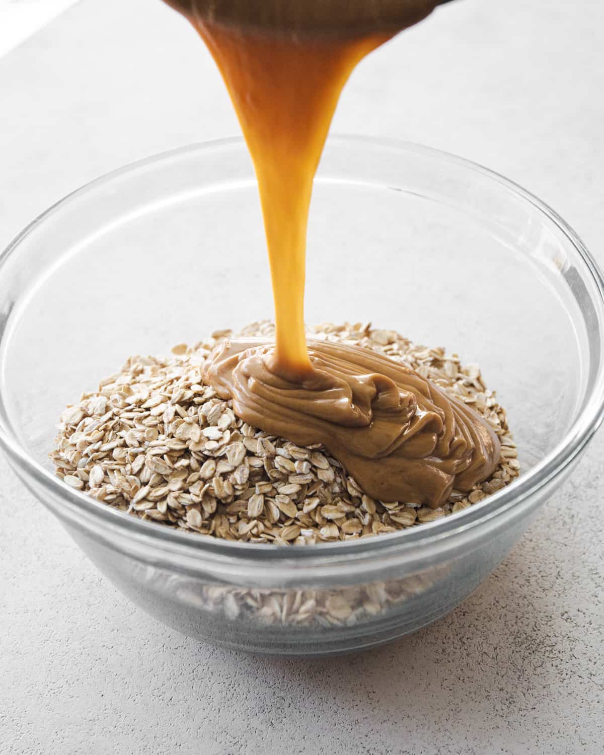 pouring peanut butter over oats in a glass mixing bowl