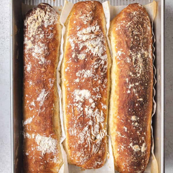 three rustic no-knead baguettes in a 9x13 pan, divided with parchment