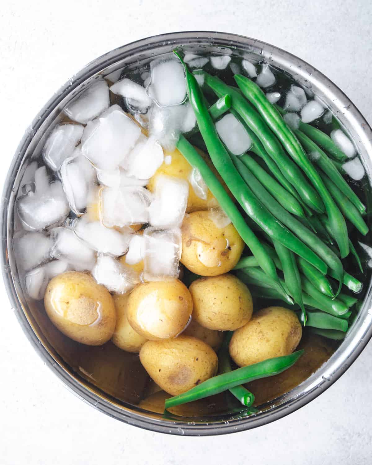 green beans and potatoes in a metal mixing bowl with ice