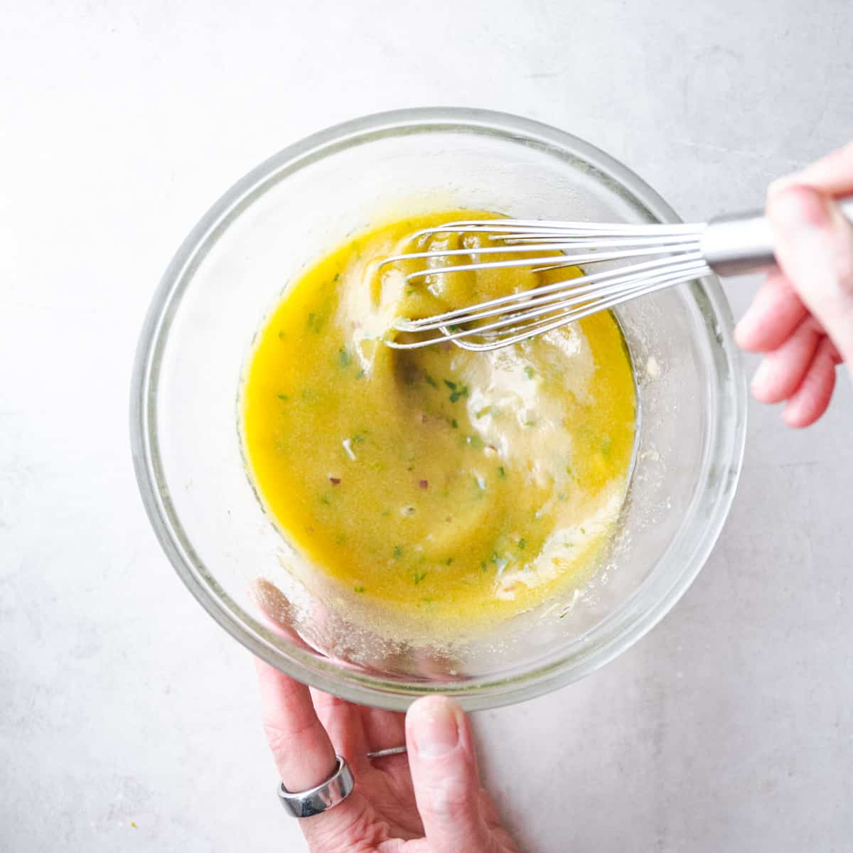 stirring ingredients for tuna salad in a clear glass mixing bowl