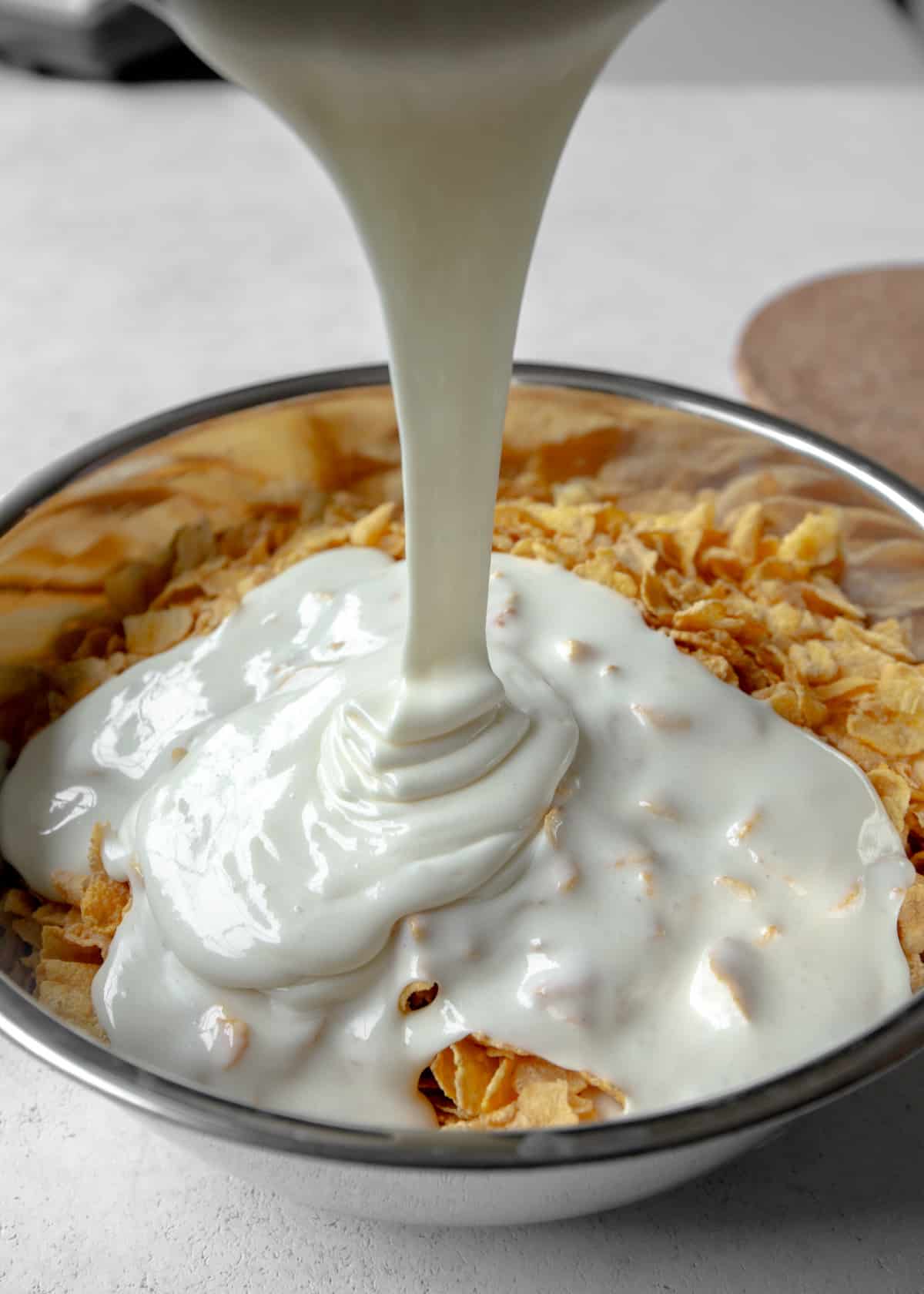 adding marshmallow mixture to cornflakes in a metal mixing bowl