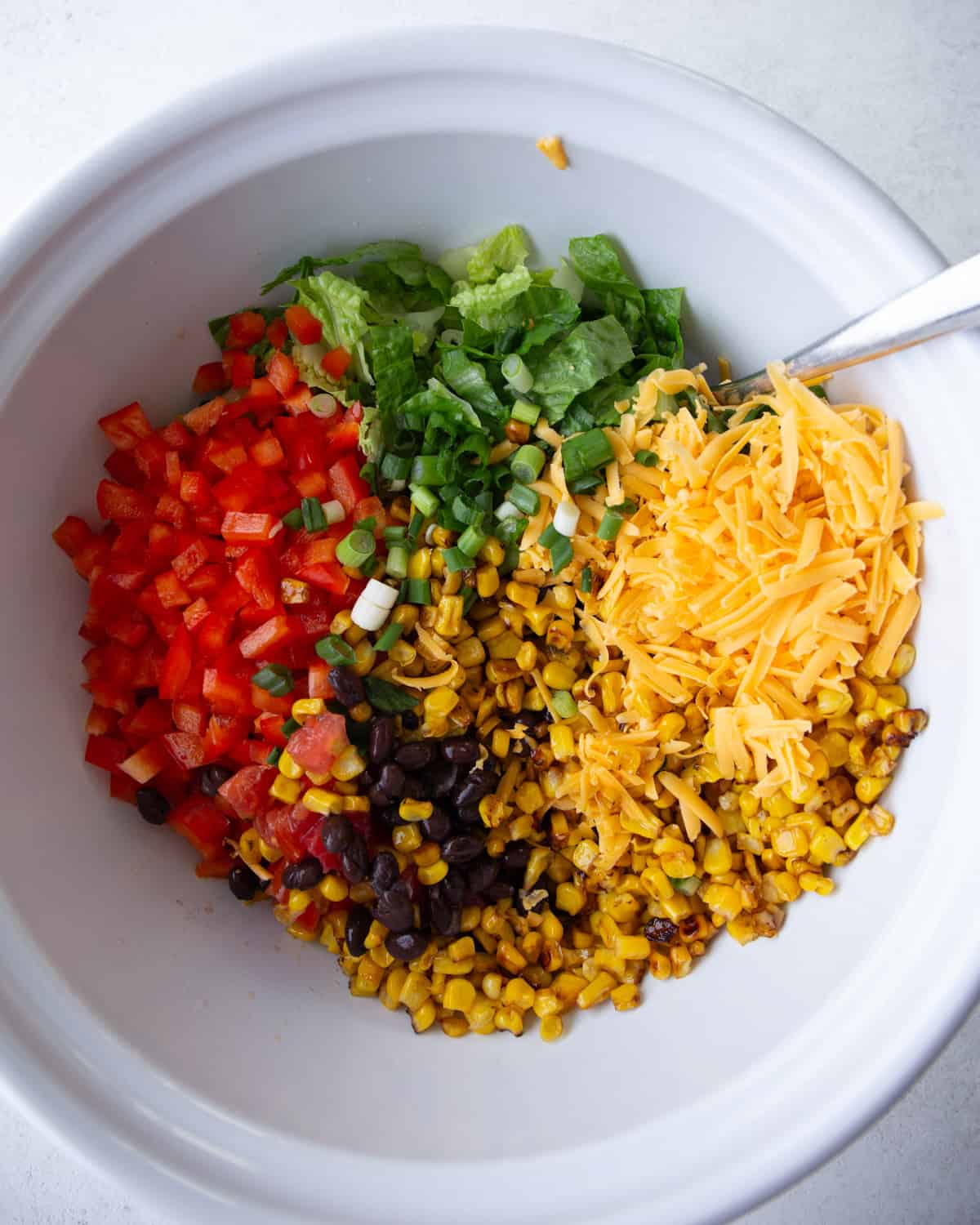 stirring ingredients for tex mex salad in a white bowl