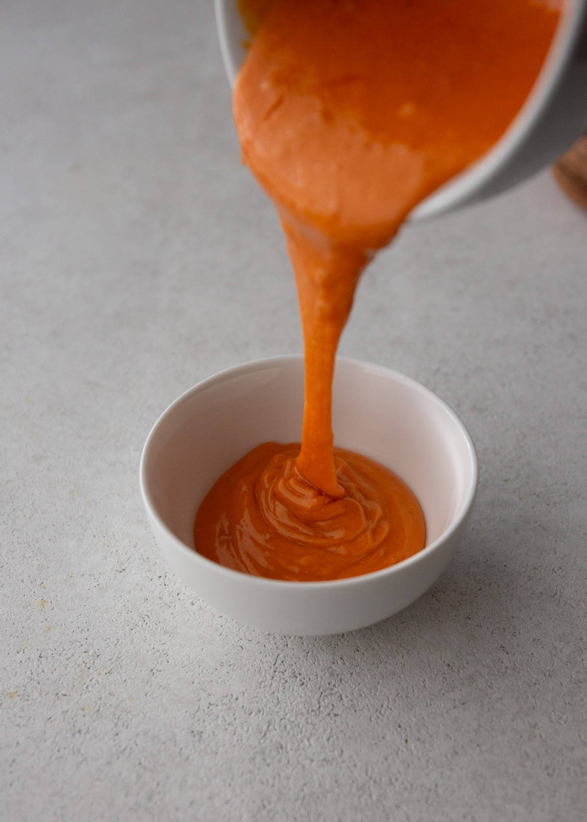 pouring sauce into a small white ramekin
