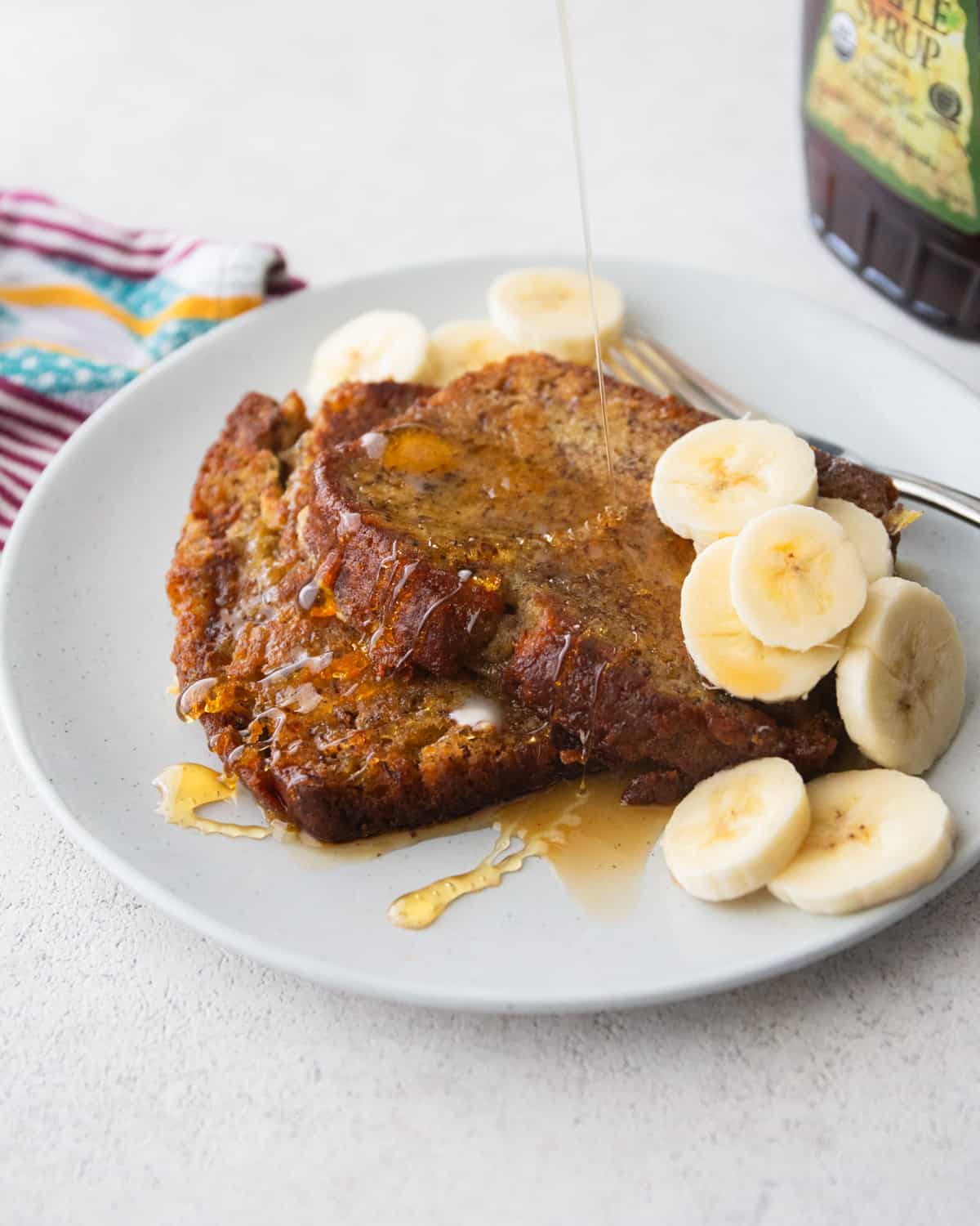drizzling syrup on banana bread french toast on a white plate