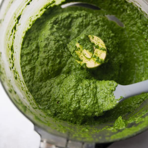 a food processor filled with spinach pesto and a gray spatula