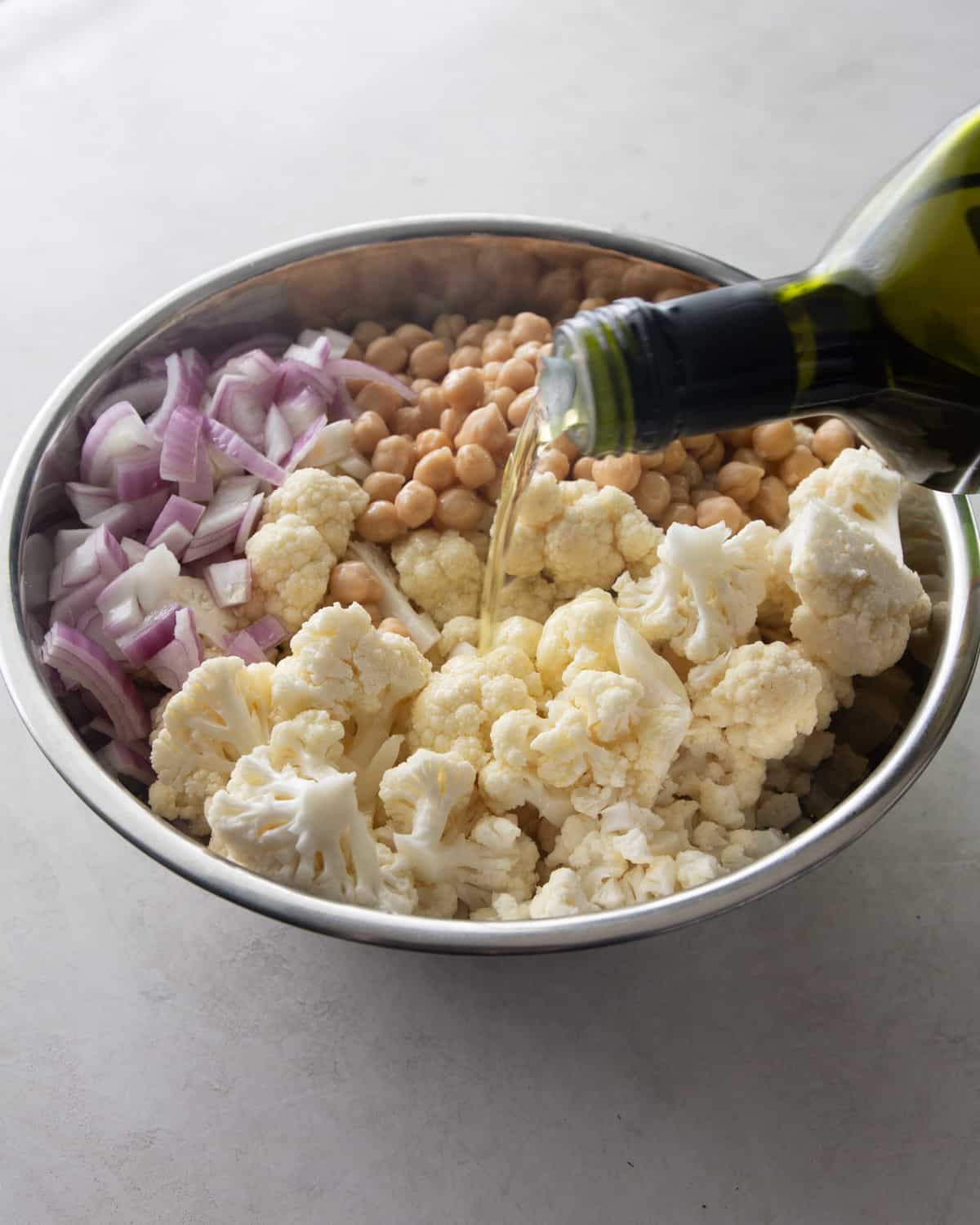 adding olive oil to cauliflower ingredients in a metal bowl