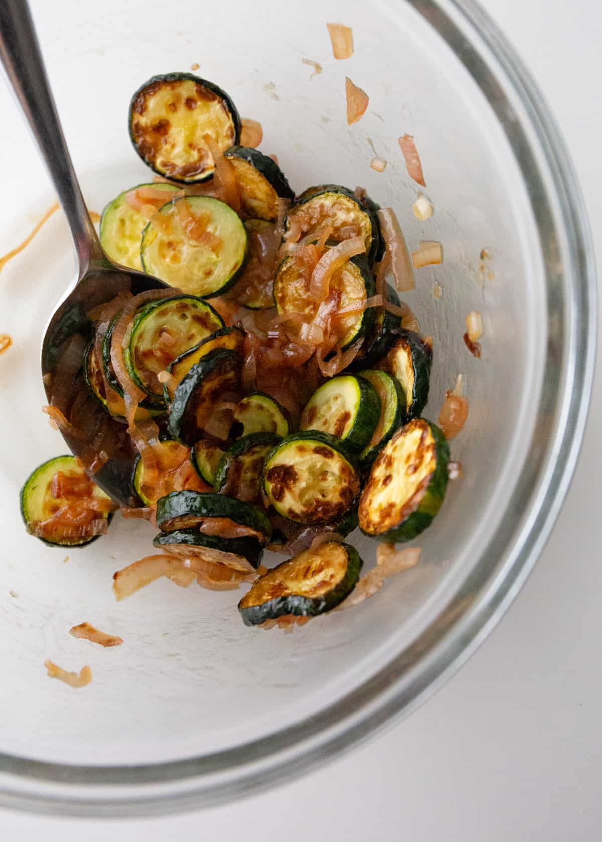 stirring roasted zucchini slices and spices in a clear glass bowl