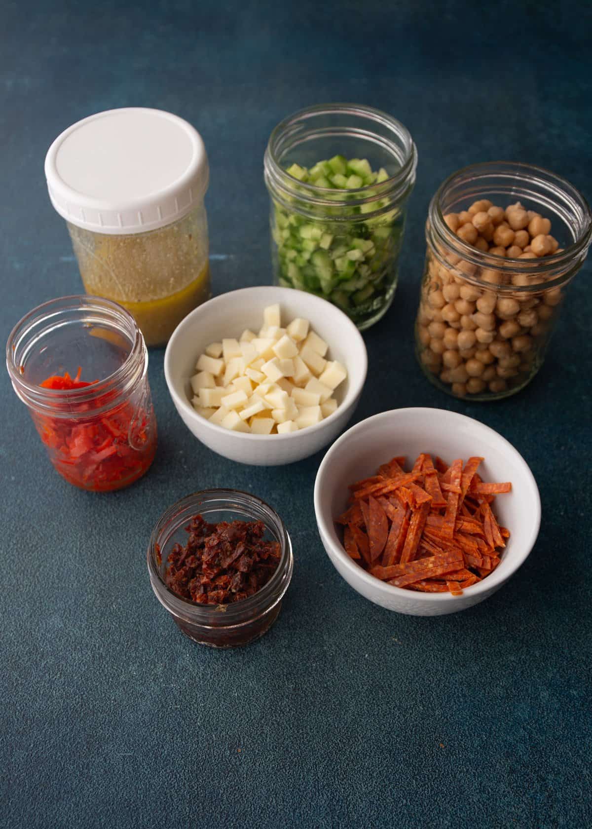 ingredients for pizza salad in glass jar on a grey countertop