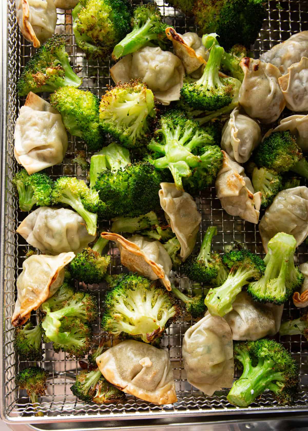 cooked broccoli and potstickers in an air fryer basket