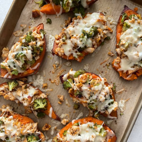 overhead image of chicken and broccoli stuffed sweet potatoes on a parchment lined sheet pan