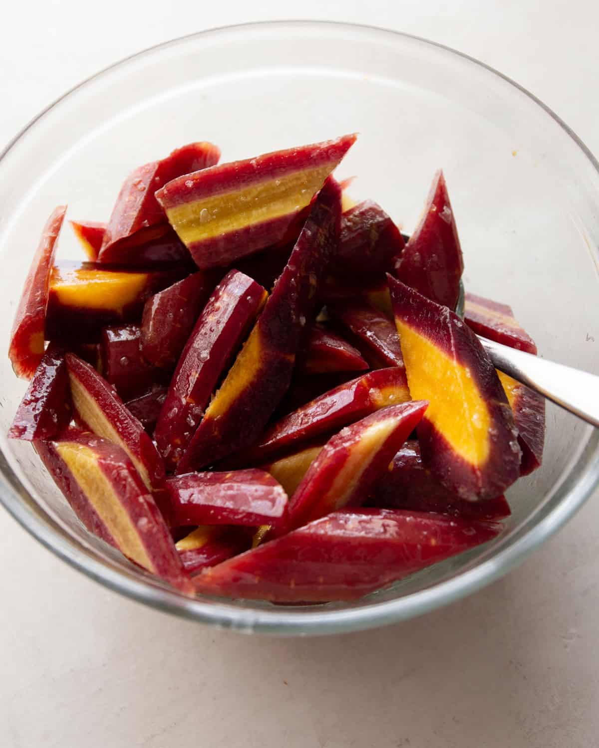 raw purple carrots in a clear glass mixing bowl