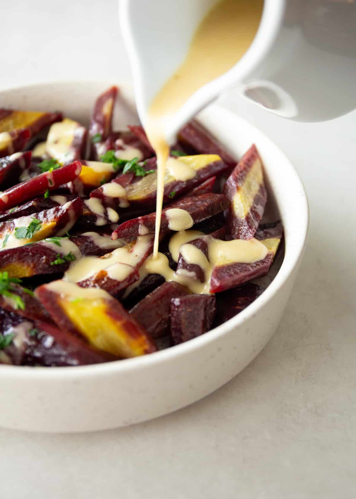 pouring honey dijon sauce over roasted rainbow carrots