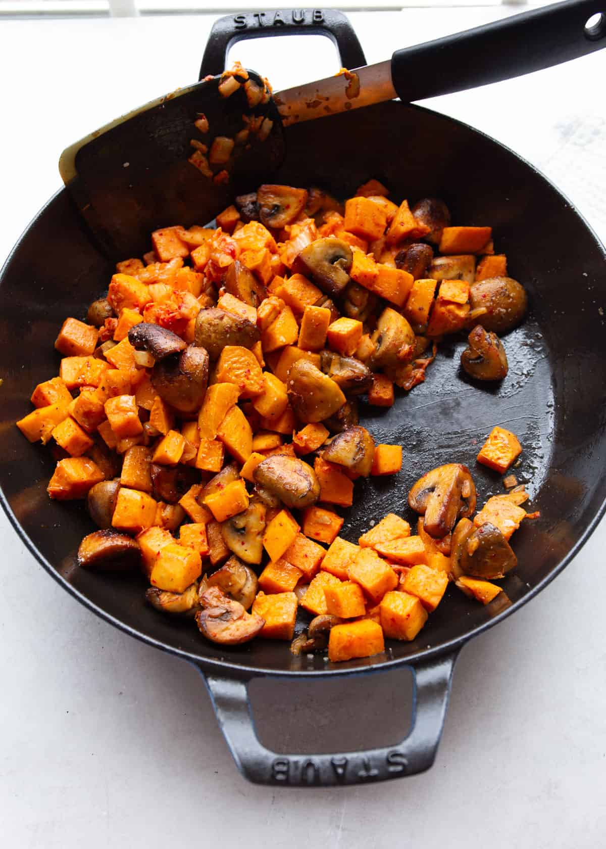 stirring sweet potatoes and mushrooms in a cast iron skillet