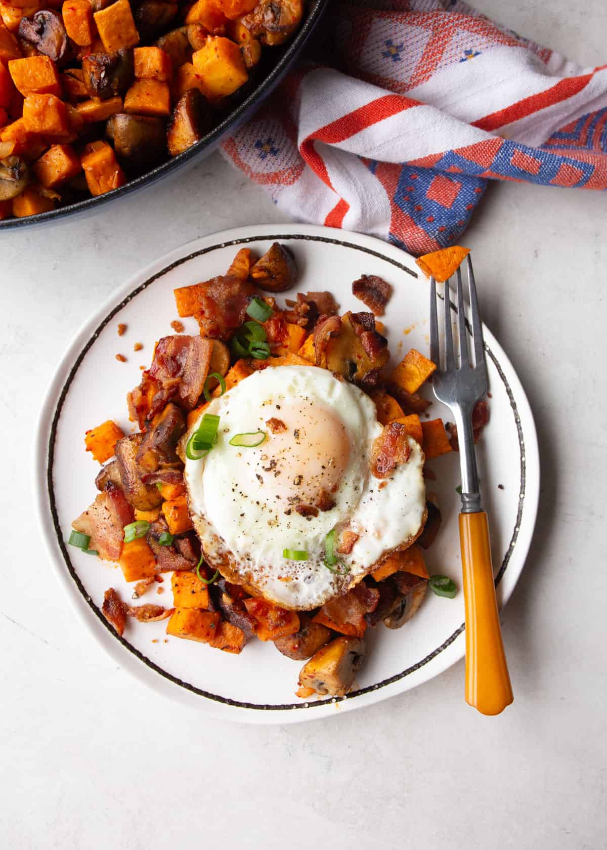 overhead image of sweet potato hash topped with a fried egg on a white plate