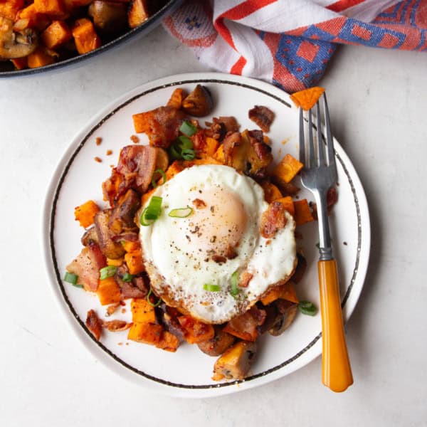 overhead image of sweet potato hash topped with a fried egg on a white plate