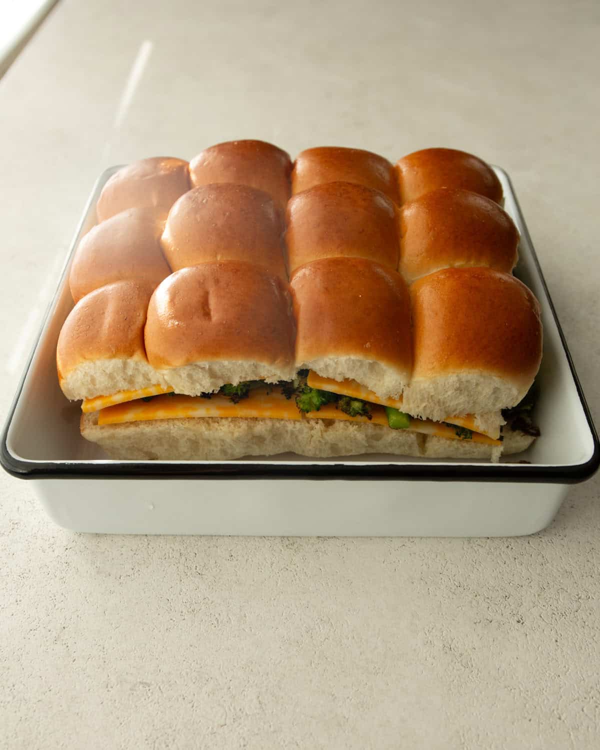 uncooked broccoli and cheese sliders in a white baking pan