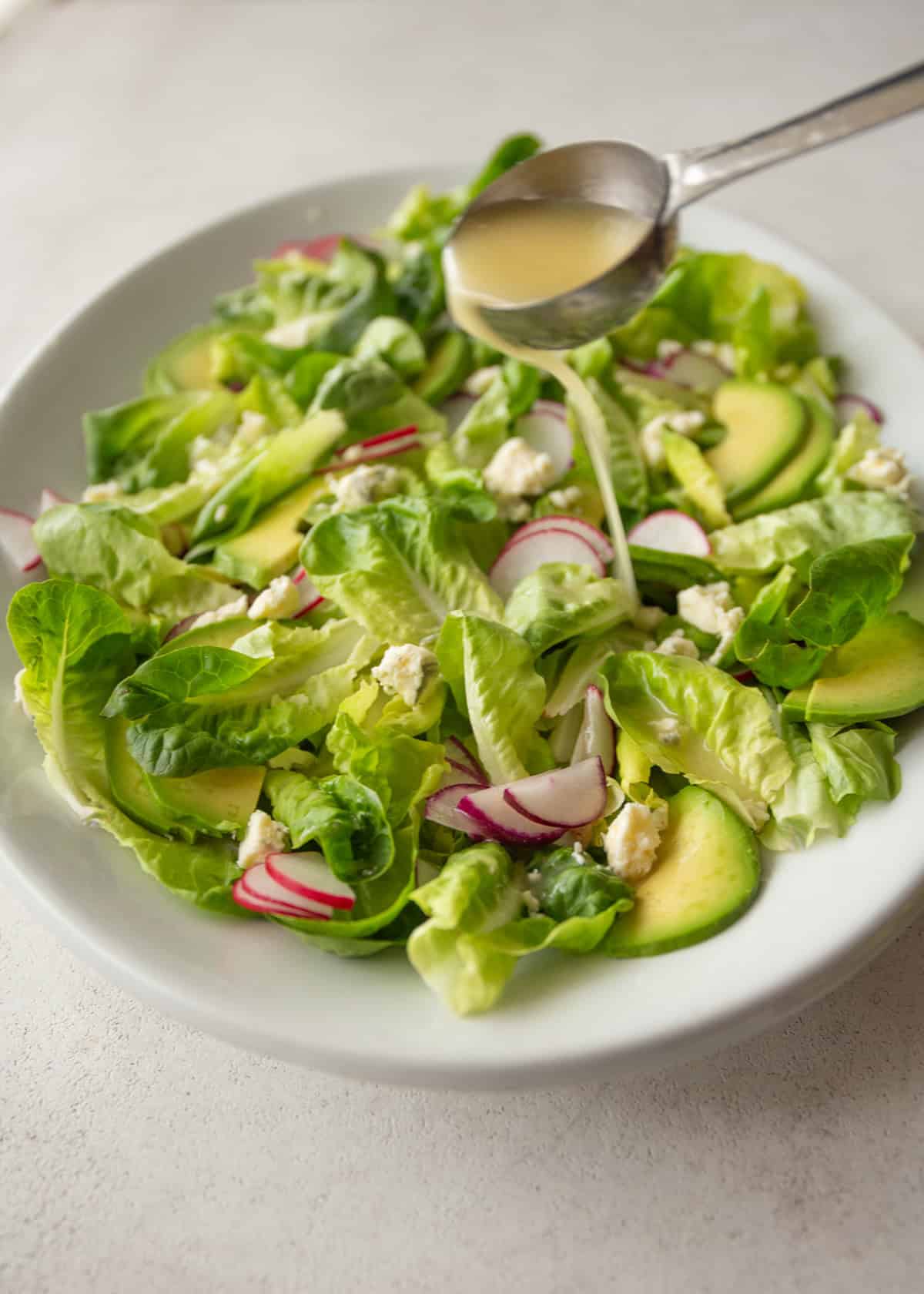 pouring vinaigrette over butter lettuce salad
