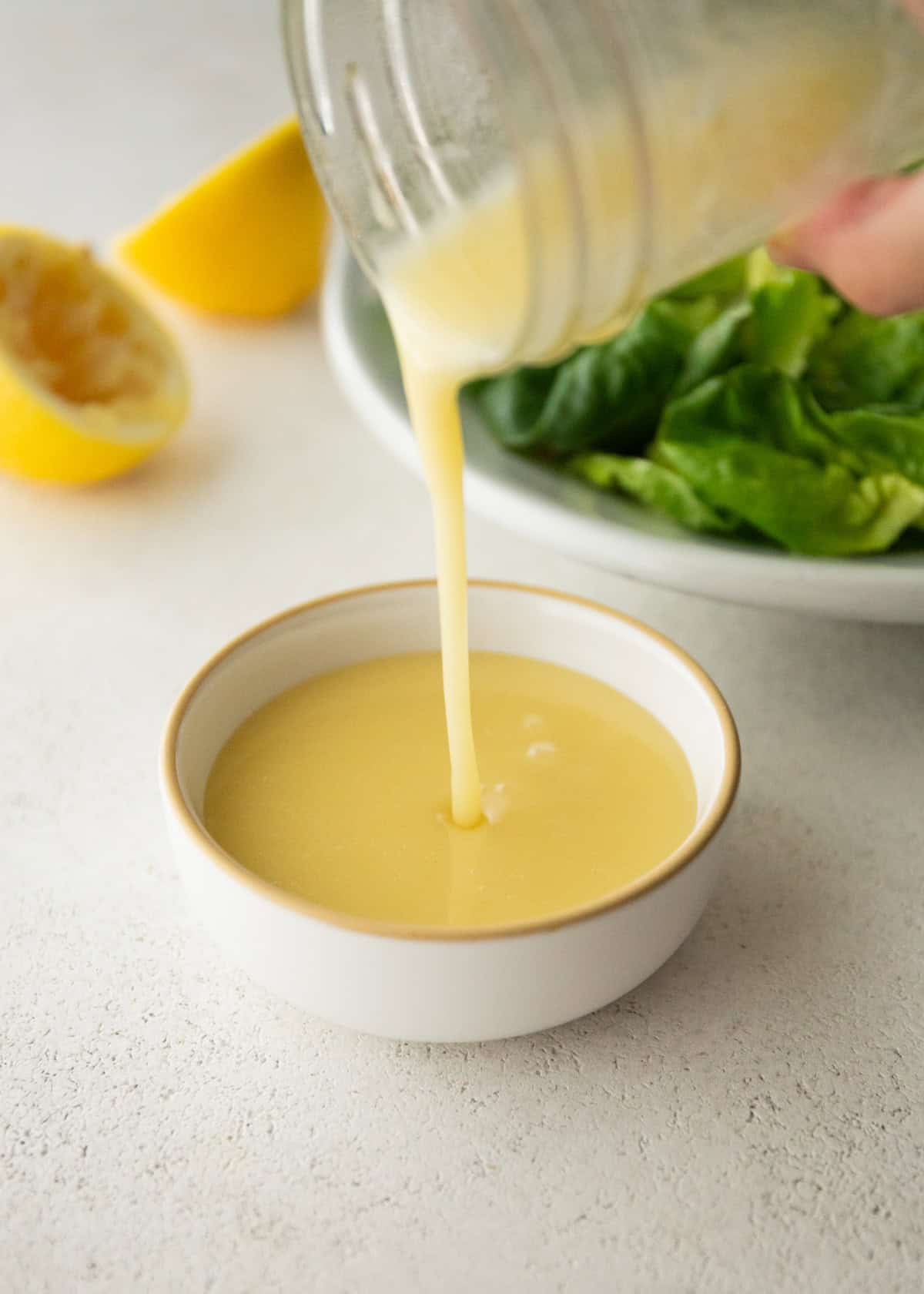 pouring lemon vinaigrette from a small glass jar into a white bowl