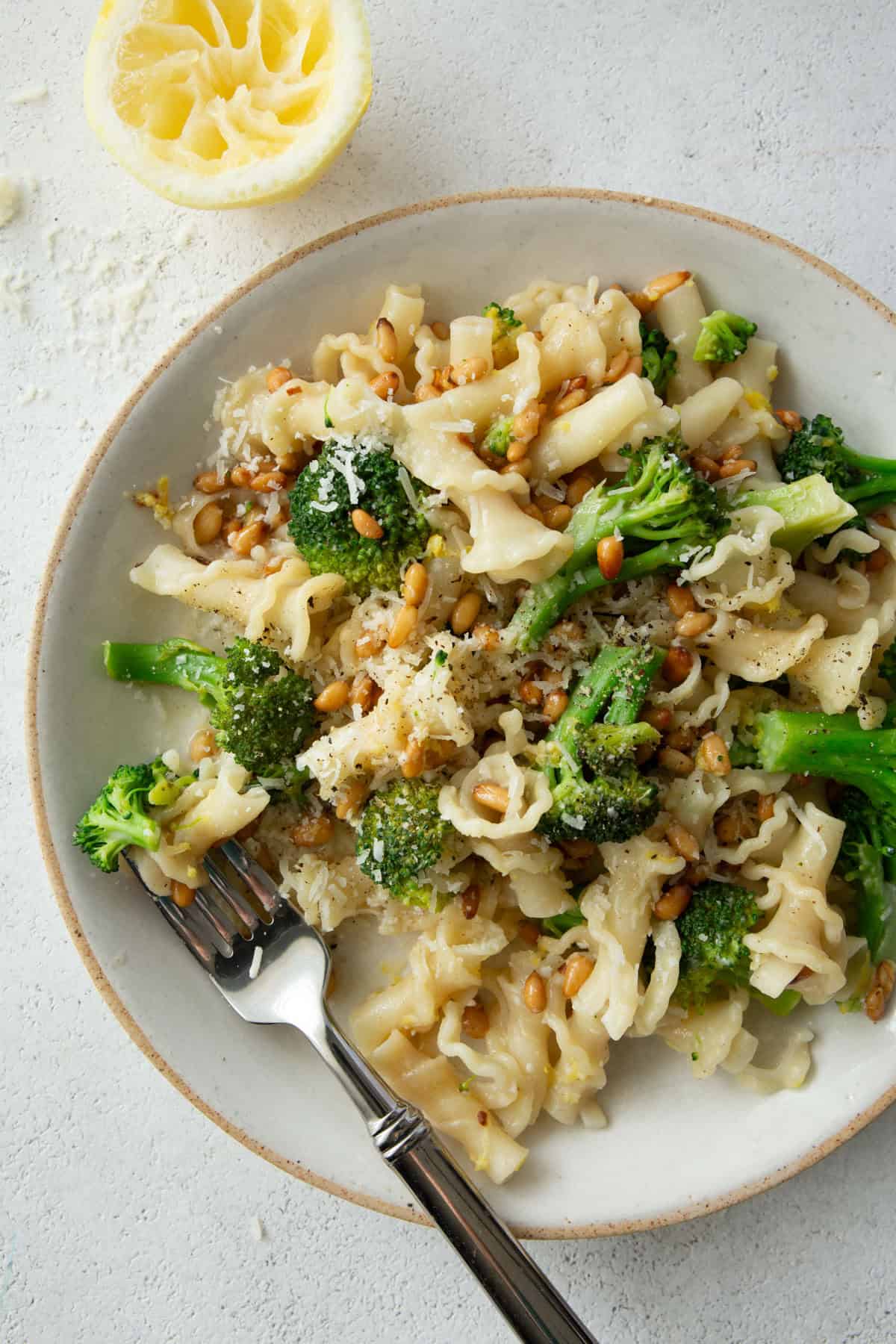 overhead image of broccoli pasta on a white plate next to a lemon half