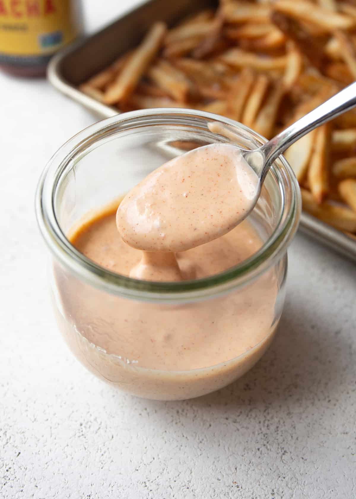 a spoon in a small bowl of yum yum sauce on a grey countertop