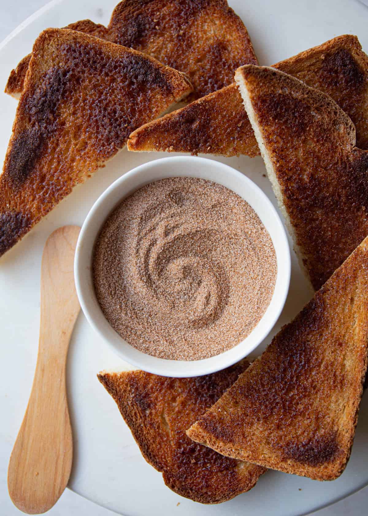 overhead image of cinnamon sugar in a white ramekin next to triangular pieces of cinnamon toast