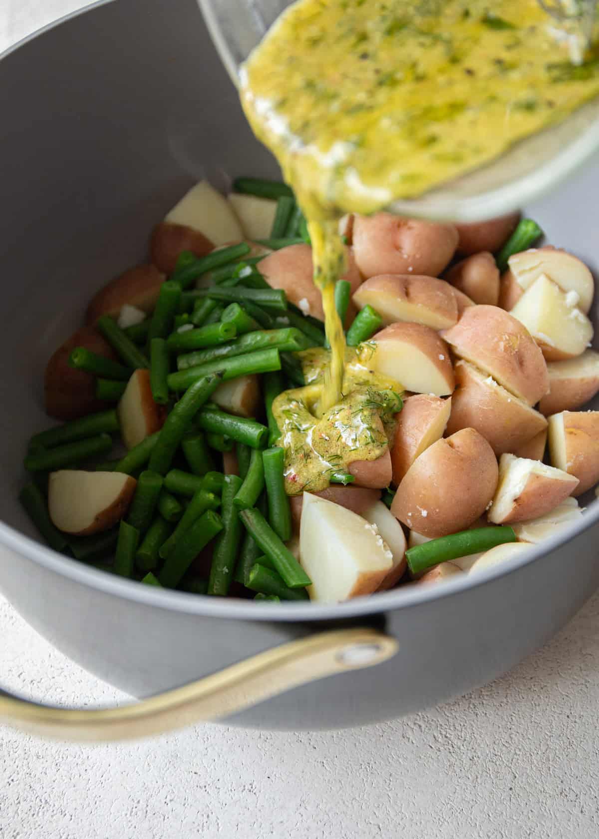 pouring dressing over cooked potatoes and green beans in a dutch oven
