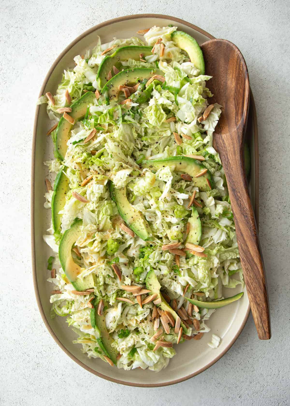 overhead image of salad on an oval plate with a wooden spoon
