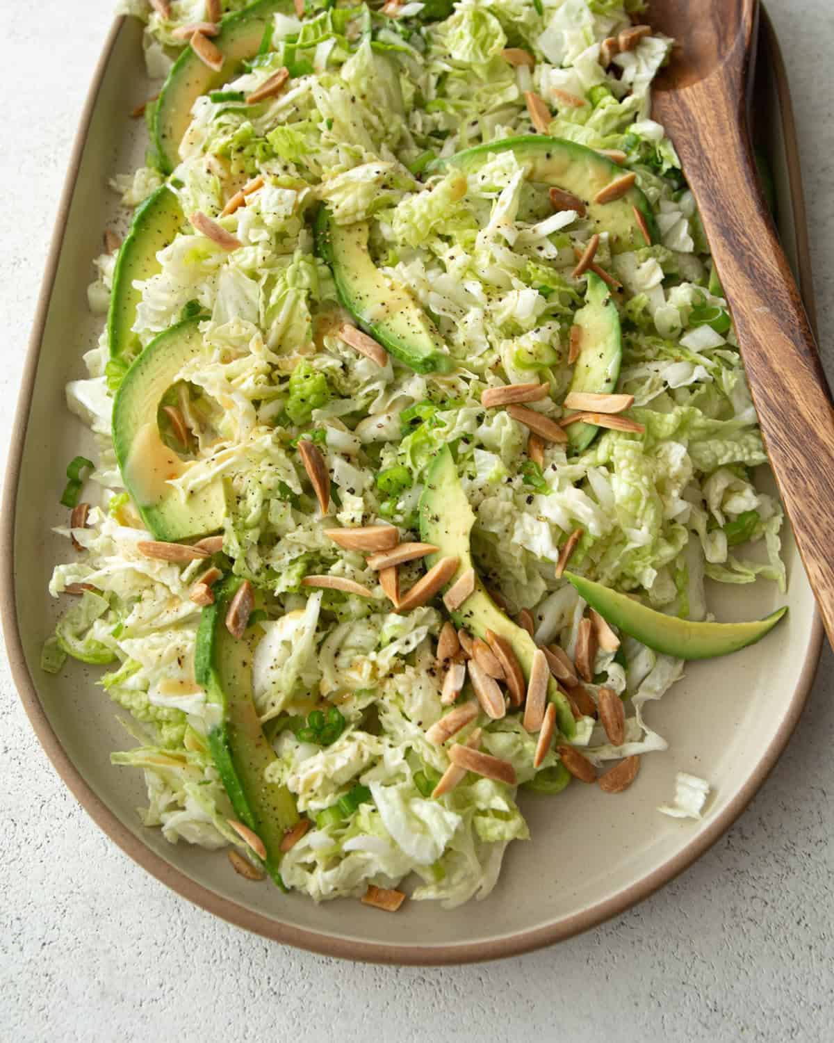 Napa Cabbage salad on a white plate with a wooden spoon