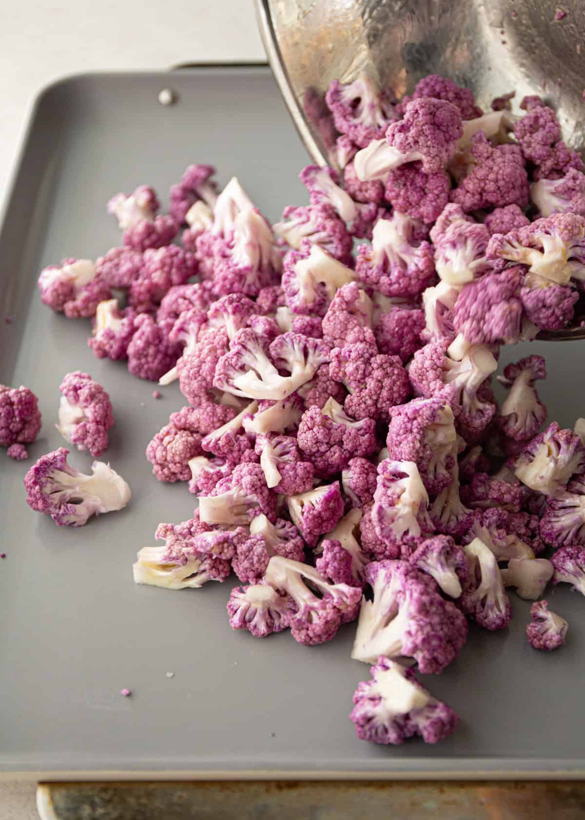 pouring raw purple cauliflower florets onto a sheet pan