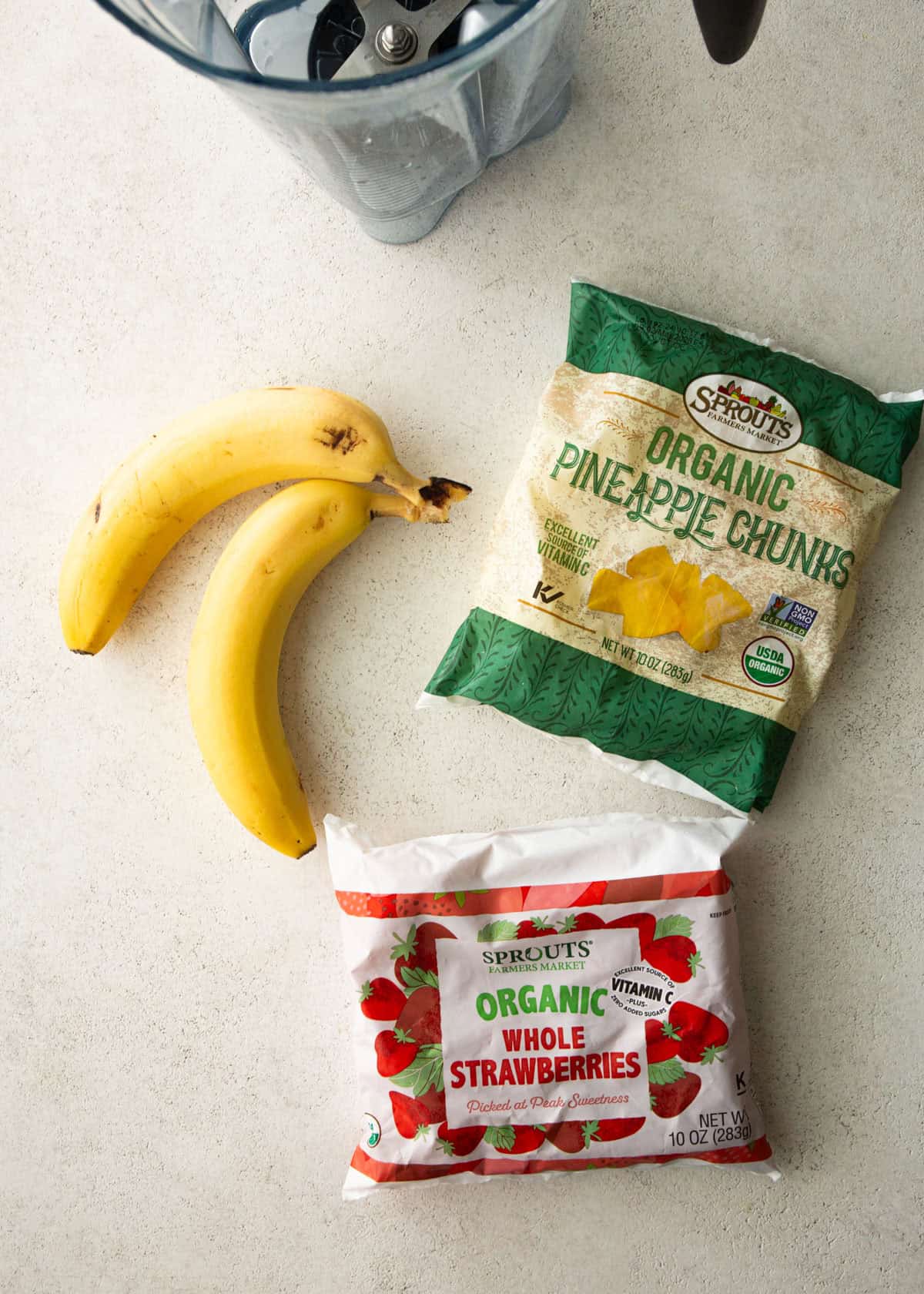 overhead image of frozen pineapple, frozen strawberries, and 2 bananas on a white countertop