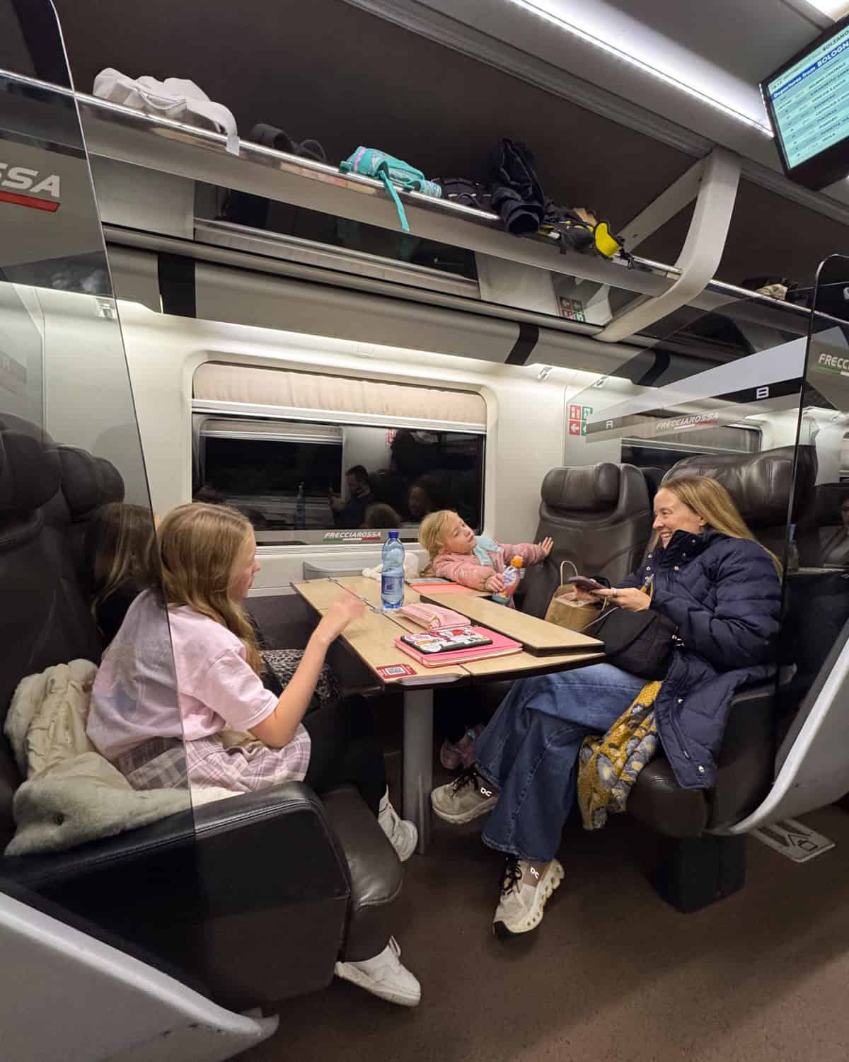 a mom and three daughters on a train with four seats facing each other with a table in between them